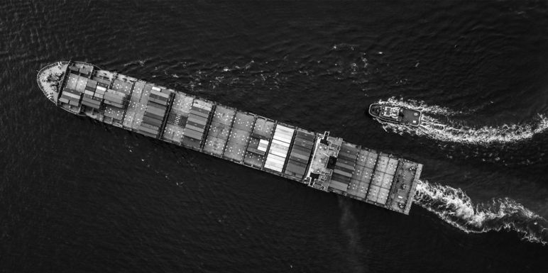Großes Containerfrachtschiff auf dem Meer, daneben ein kleineres Boot. 